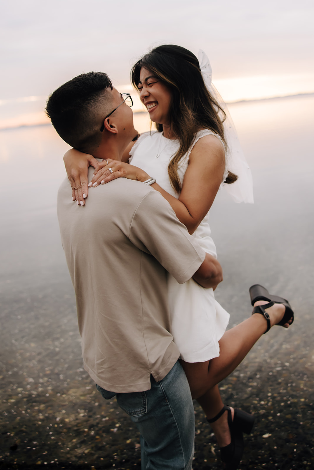 Groom to be picking up his fiance as she smiles on the beach