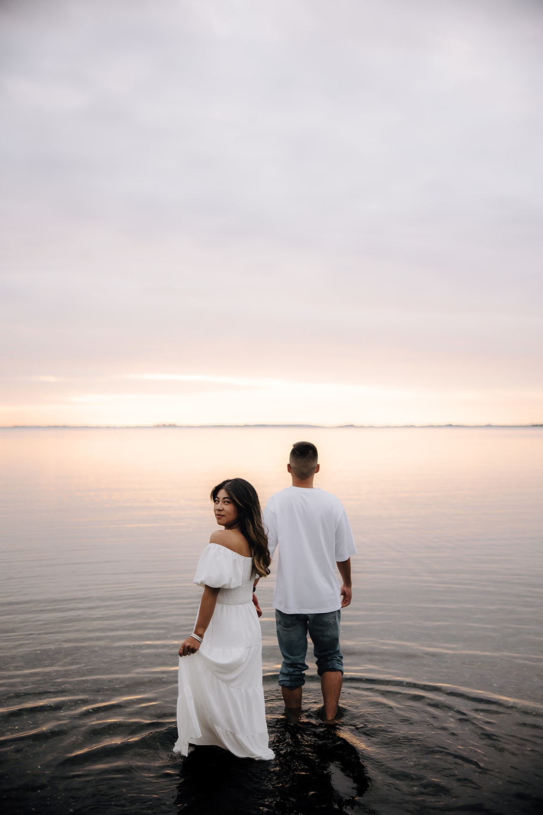 Engaged couple holding hands walking in the ocean during sunset