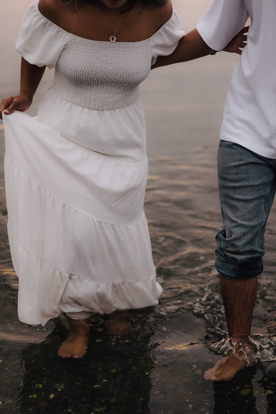 A close-up of the bride-to-be holding her dress while walking through the shallow water, her laughter reflecting the playful vibe of their beach engagement photos.