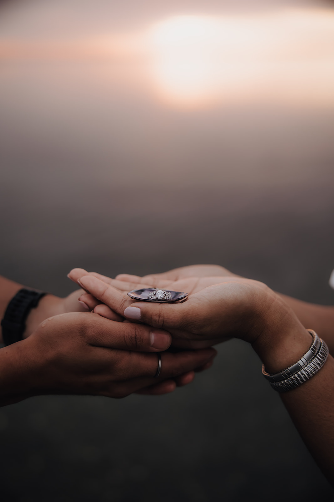 A close-up detail shot of the couple's engagement ring resting in their hands, set against the backdrop of the soft evening light at the beach.