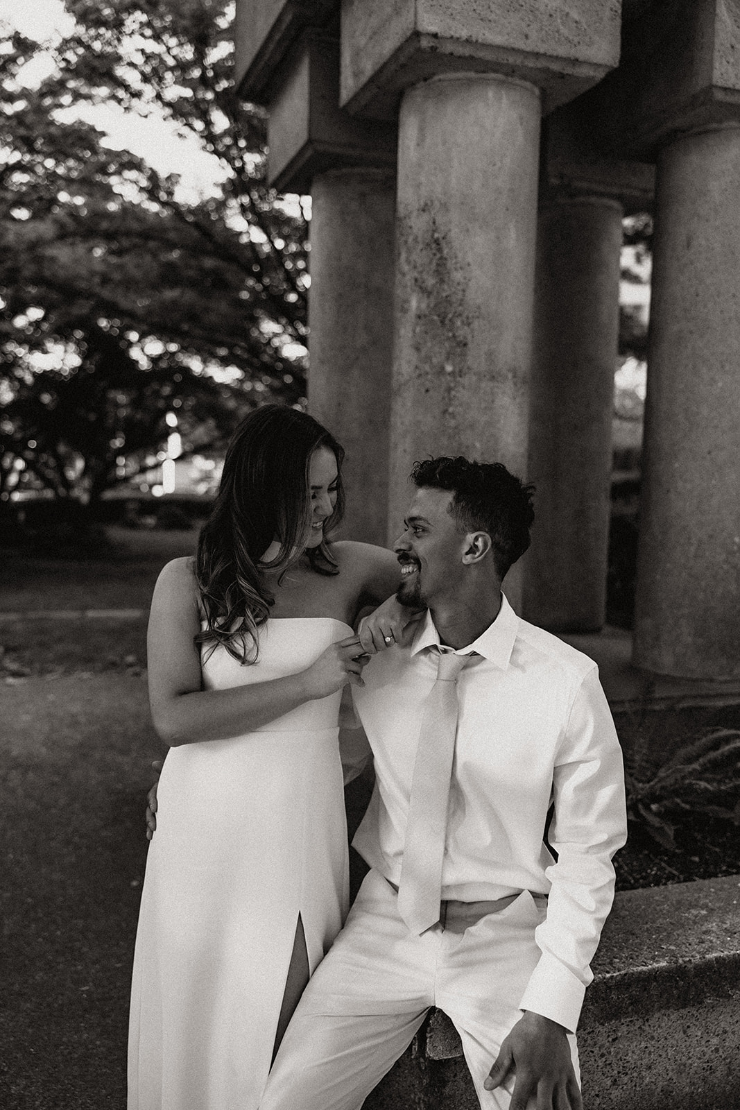 Black and white photo of a couple laughing together in front of concrete columns.