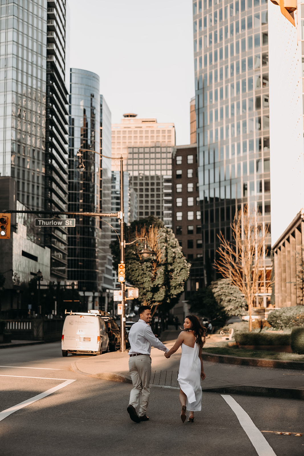 A couple walking hand in hand across a busy intersection, with the city skyline towering behind them.