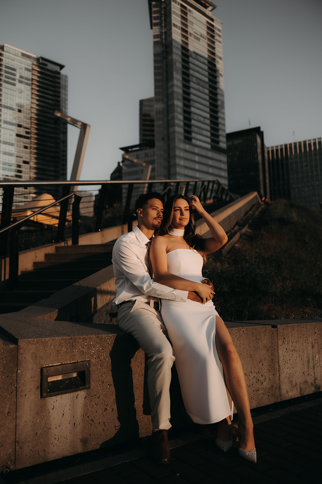 A couple seated on concrete steps, gazing at the cityscape during their downtown engagement session.