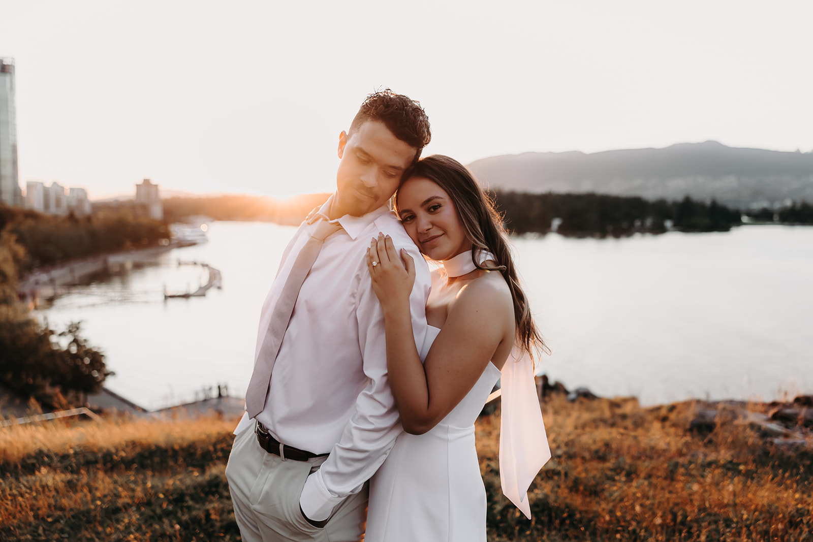 A couple embraces during sunset with the city skyline in the background, capturing the warmth and romance of downtown engagement photos.