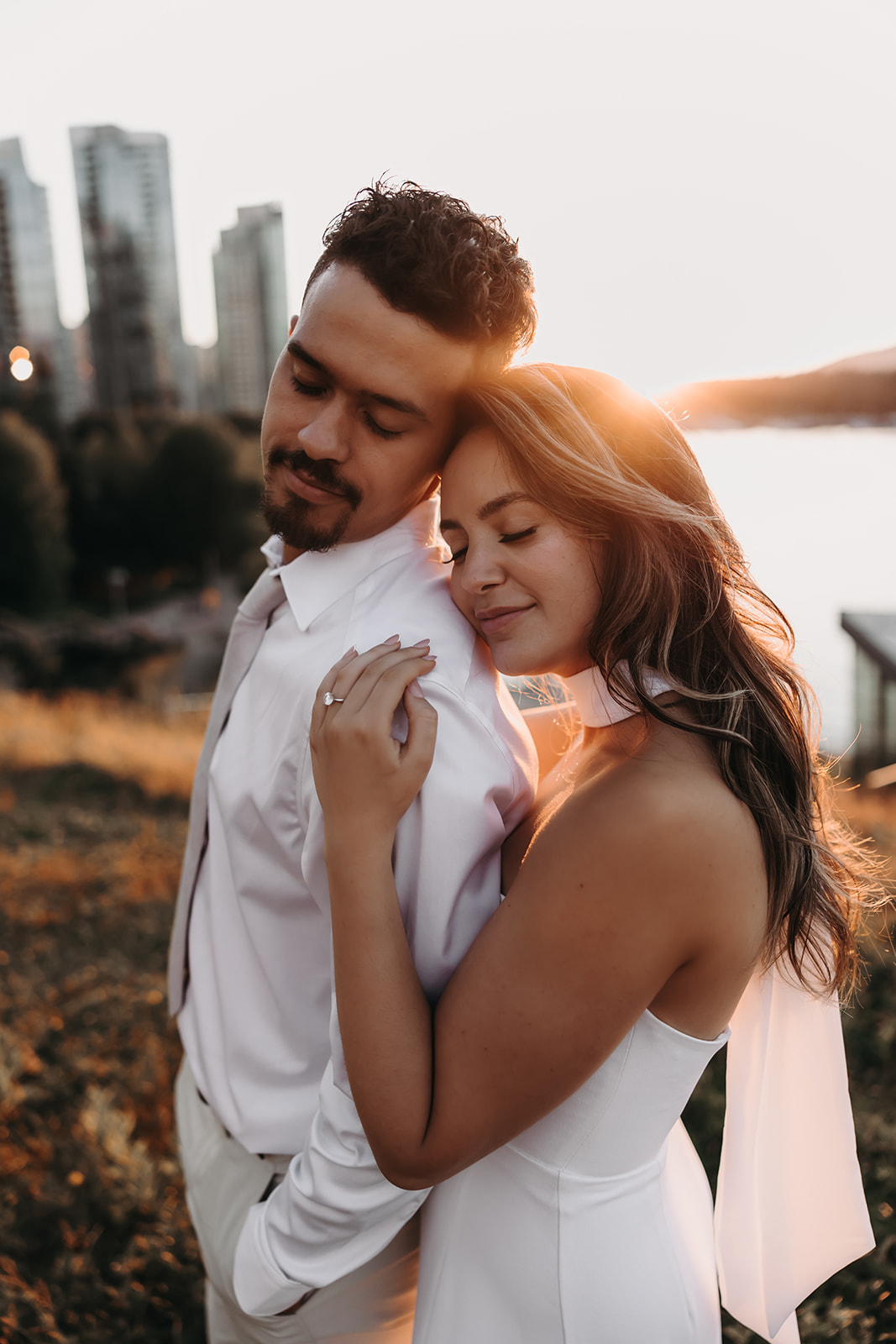 A couple embraces during sunset with the city skyline in the background, capturing the warmth and romance of downtown engagement photos.