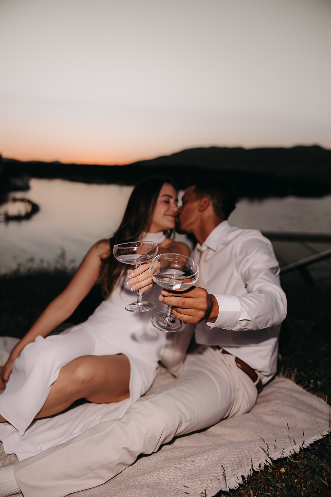 A couple toasting at sunset while sharing an intimate kiss during their downtown engagement photoshoot by the water.