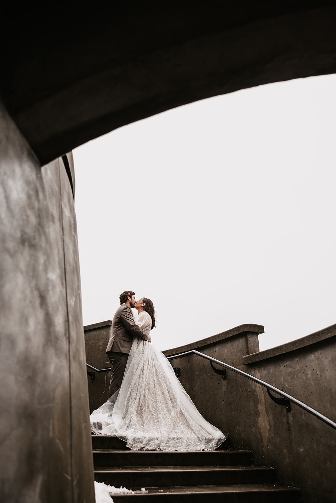 The newlyweds embrace on the steps, with the bride’s flowing gown trailing behind in this romantic moment from their Vancouver elopement.