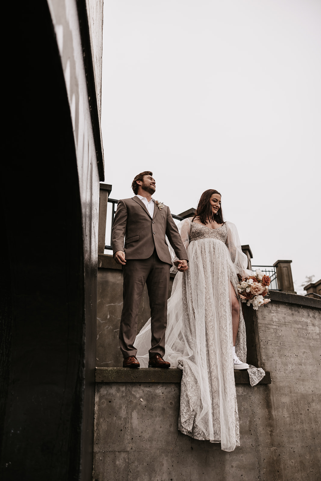 The couple holds hands as they prepare to descend the stairs, their elegant attire making a statement against the urban backdrop.