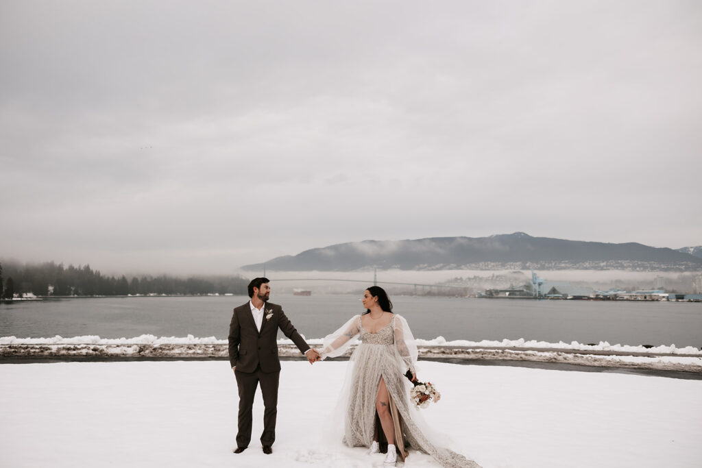 The bride and groom holding hands, looking into each other’s eyes, surrounded by snow-covered ground during their winter elopement in Vancouver.