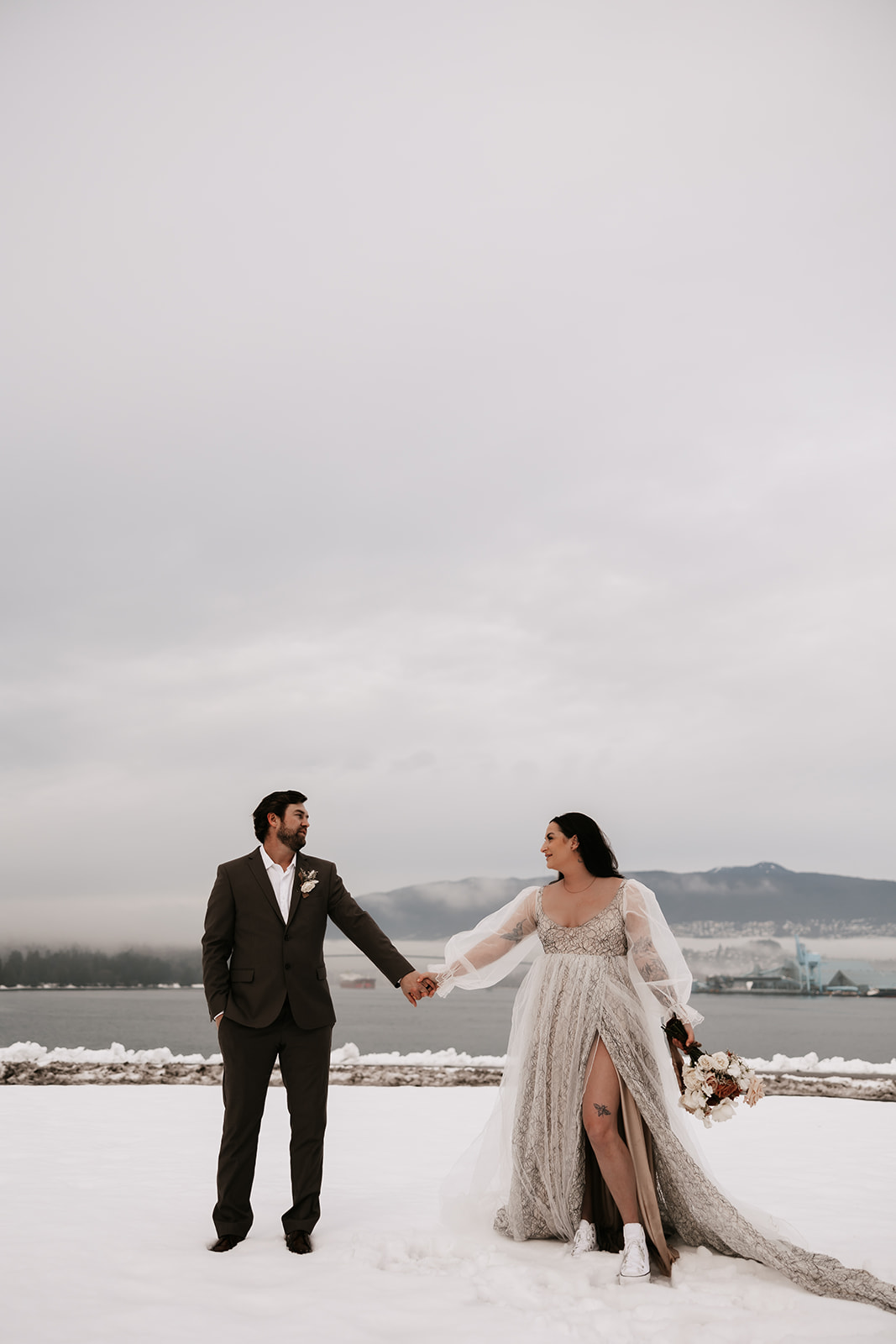 The bride and groom holding hands, looking into each other’s eyes, surrounded by snow-covered ground during their winter elopement in Vancouver.