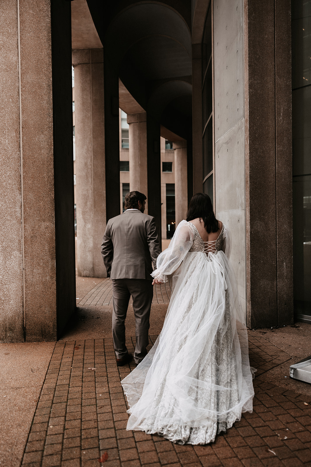 The bride and groom holding hands, standing under the architectural details of downtown Vancouver during their chic city elopement.