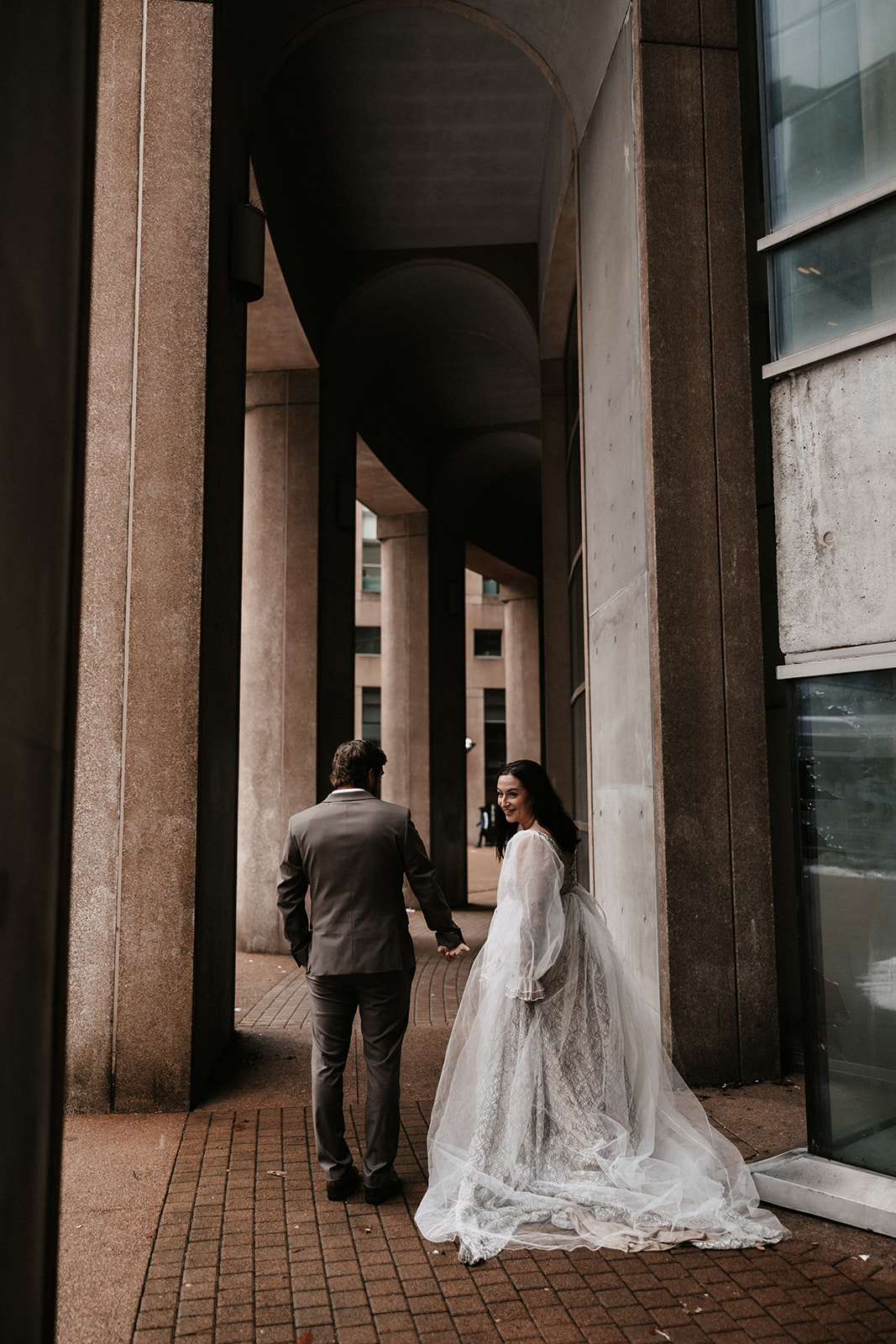 The bride and groom holding hands, standing under the architectural details of downtown Vancouver during their chic city elopement.