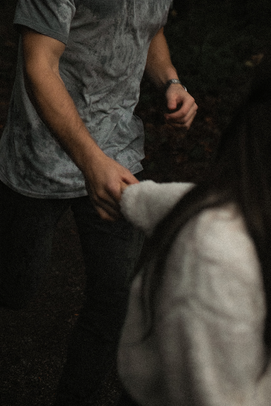 A couple's hands intertwined, showcasing their connection amidst a backdrop of trees. The image is taken during a rainy day couple shoot, emphasizing the beauty of shared moments in the rain.