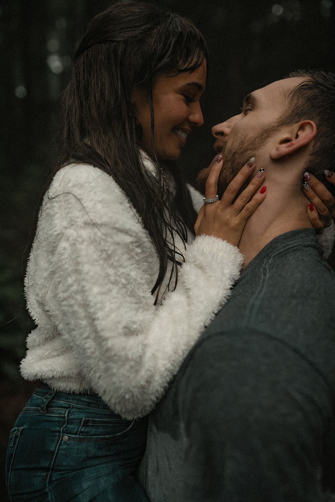 The couple leans in for another loving kiss, their faces close together as raindrops cascade down around them. The focus is on their expressions of joy and affection, making this rainy day couple picture a perfect example of how to embrace the weather for a memorable fun couple photoshoot. The greenery in the background adds a refreshing touch to the atmosphere.