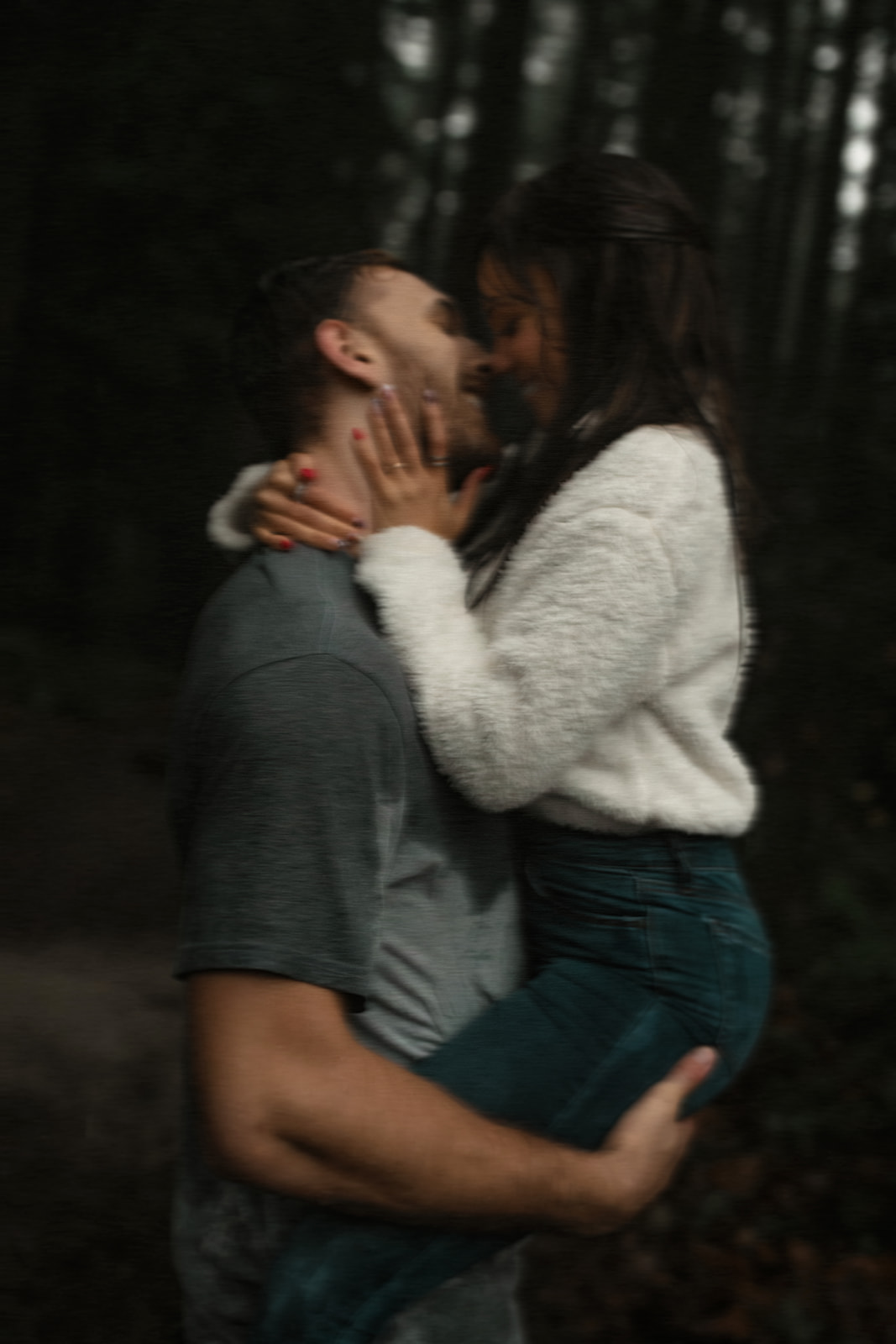 The couple leans in for another loving kiss, their faces close together as raindrops cascade down around them. The focus is on their expressions of joy and affection, making this rainy day couple picture a perfect example of how to embrace the weather for a memorable fun couple photoshoot. The greenery in the background adds a refreshing touch to the atmosphere.