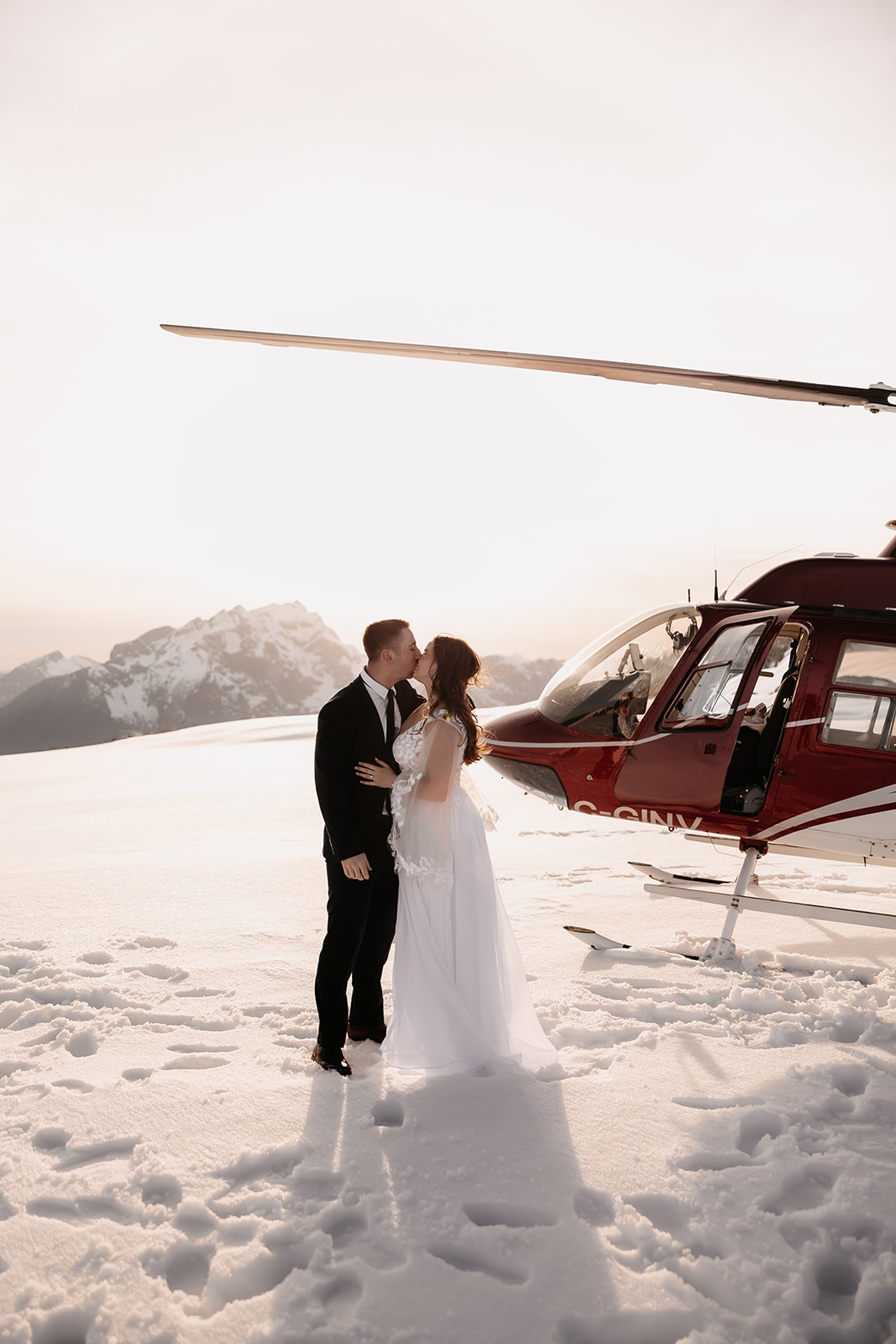 Newlyweds sharing a kiss next to their helicopter in the mountains, showcasing the beauty of their helicopter elopement.