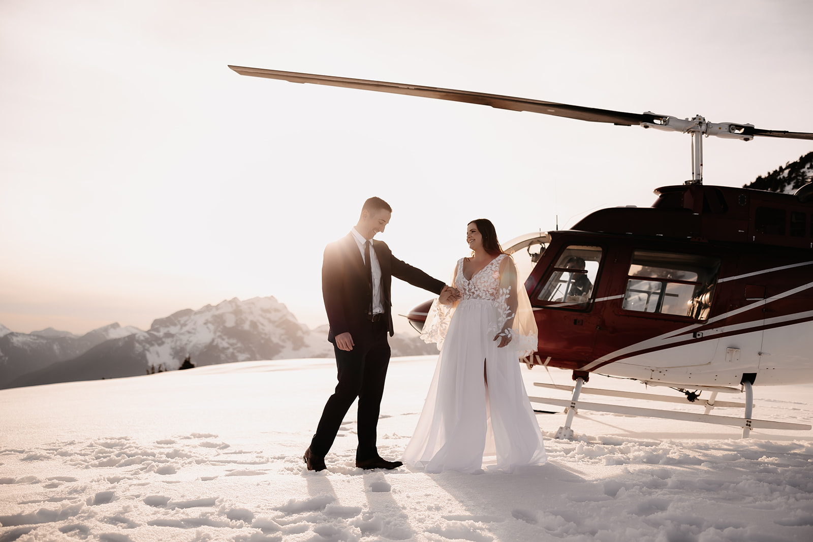 Joyful couple holding hands and dancing by their helicopter, with the breathtaking mountain scenery surrounding them.