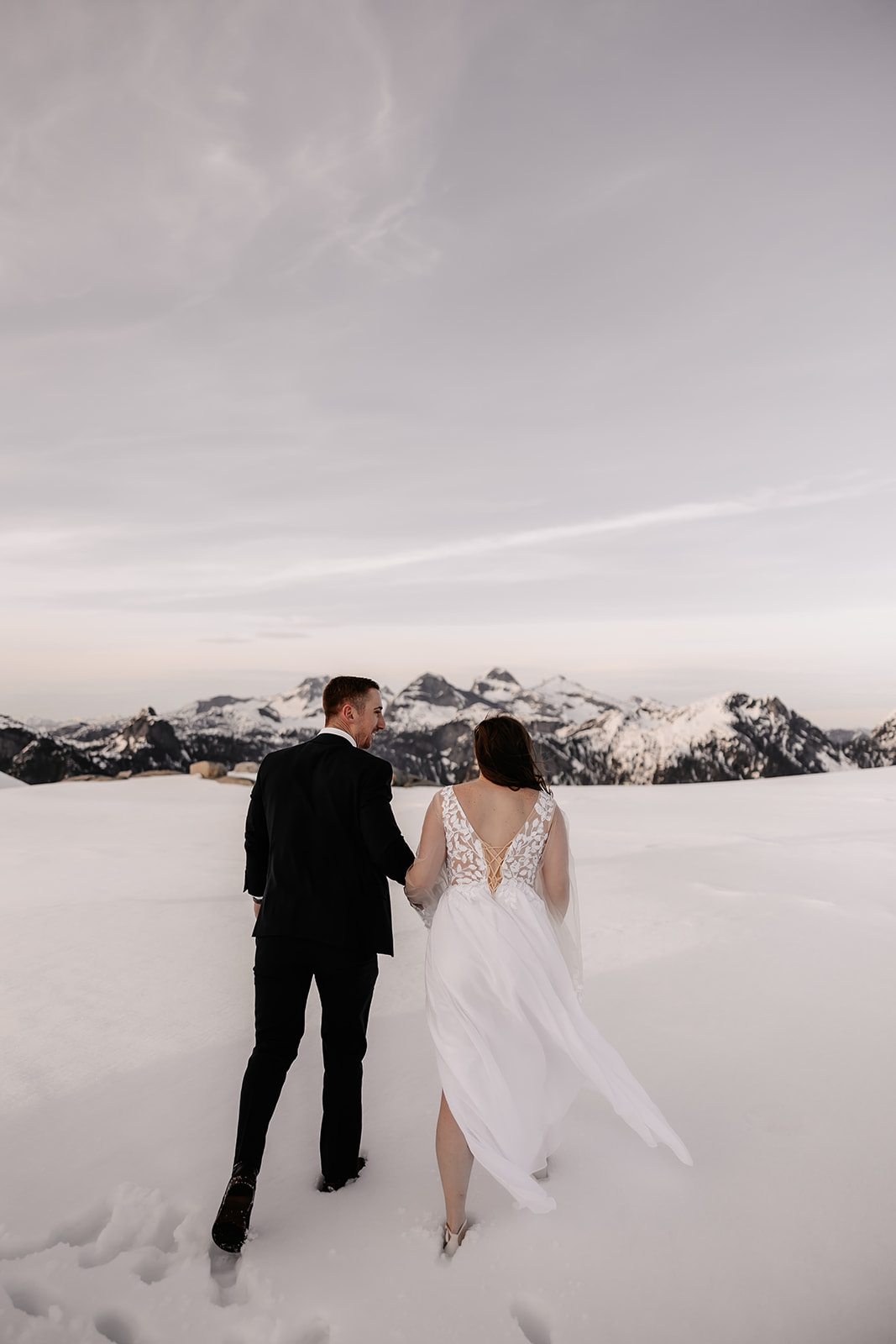 A bride and groom walking hand-in-hand through the snow, the stunning mountain landscape of BC serving as a romantic backdrop for their helicopter elopement.