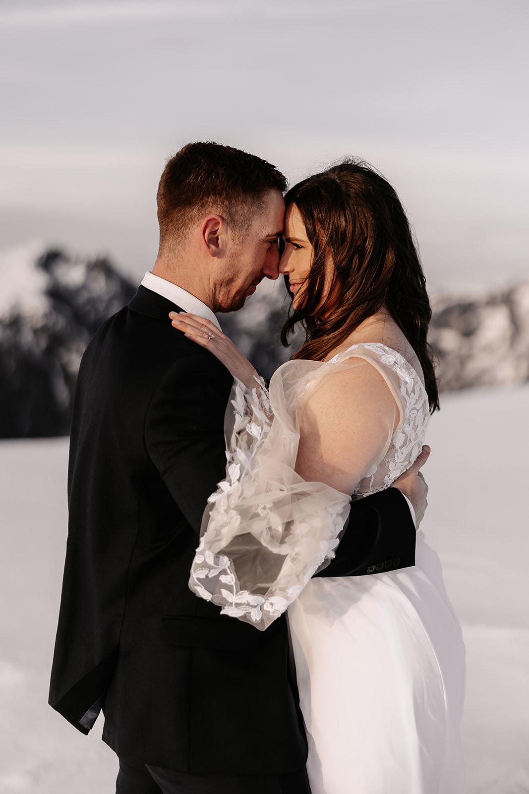 A close-up of the couple gently touching foreheads, capturing the intimate moment shared during their helicopter elopement amidst a scenic snowy landscape.