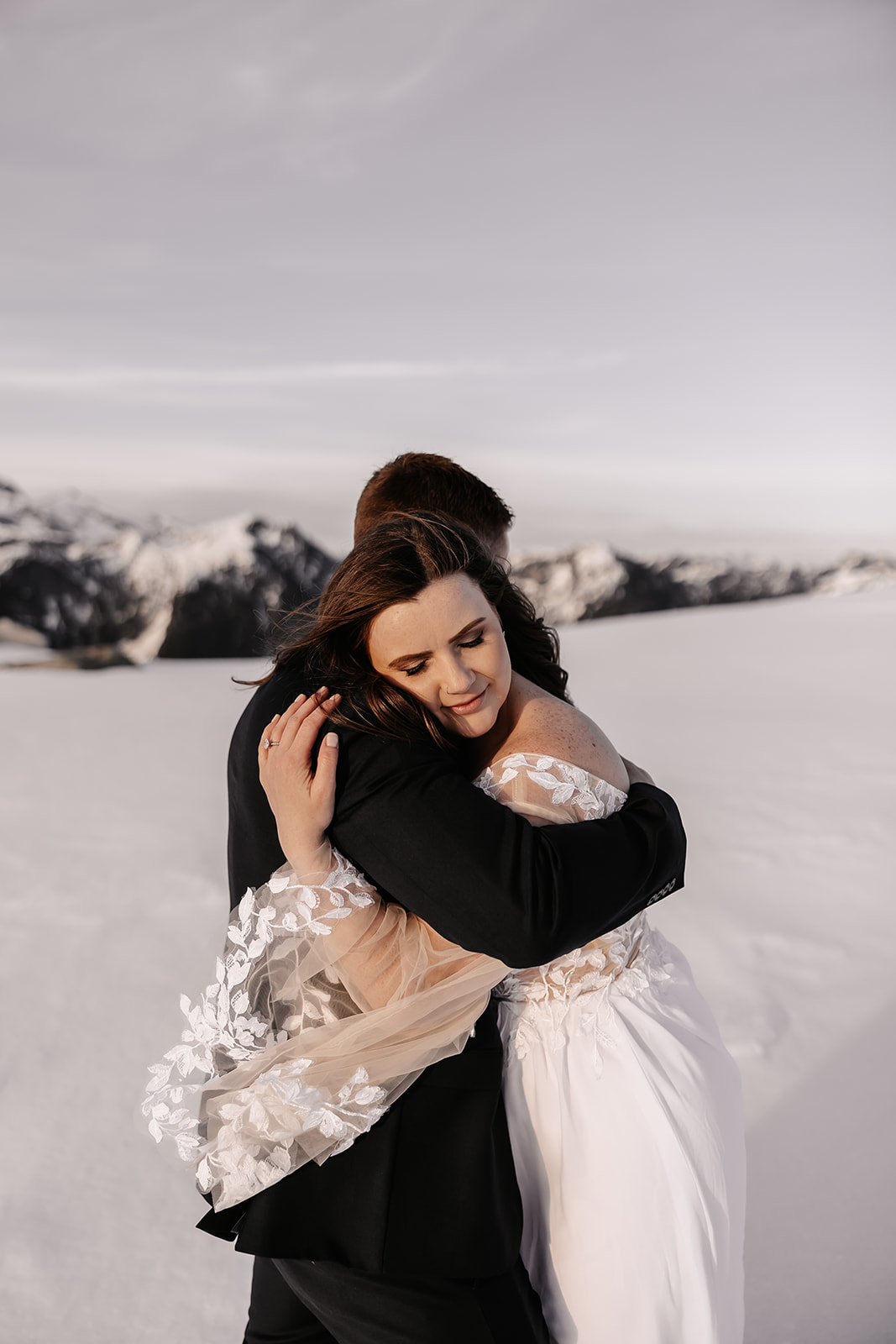 The couple embracing in the snow, with the beautiful mountain range behind them, perfectly encapsulating the love and adventure of their helicopter elopement.