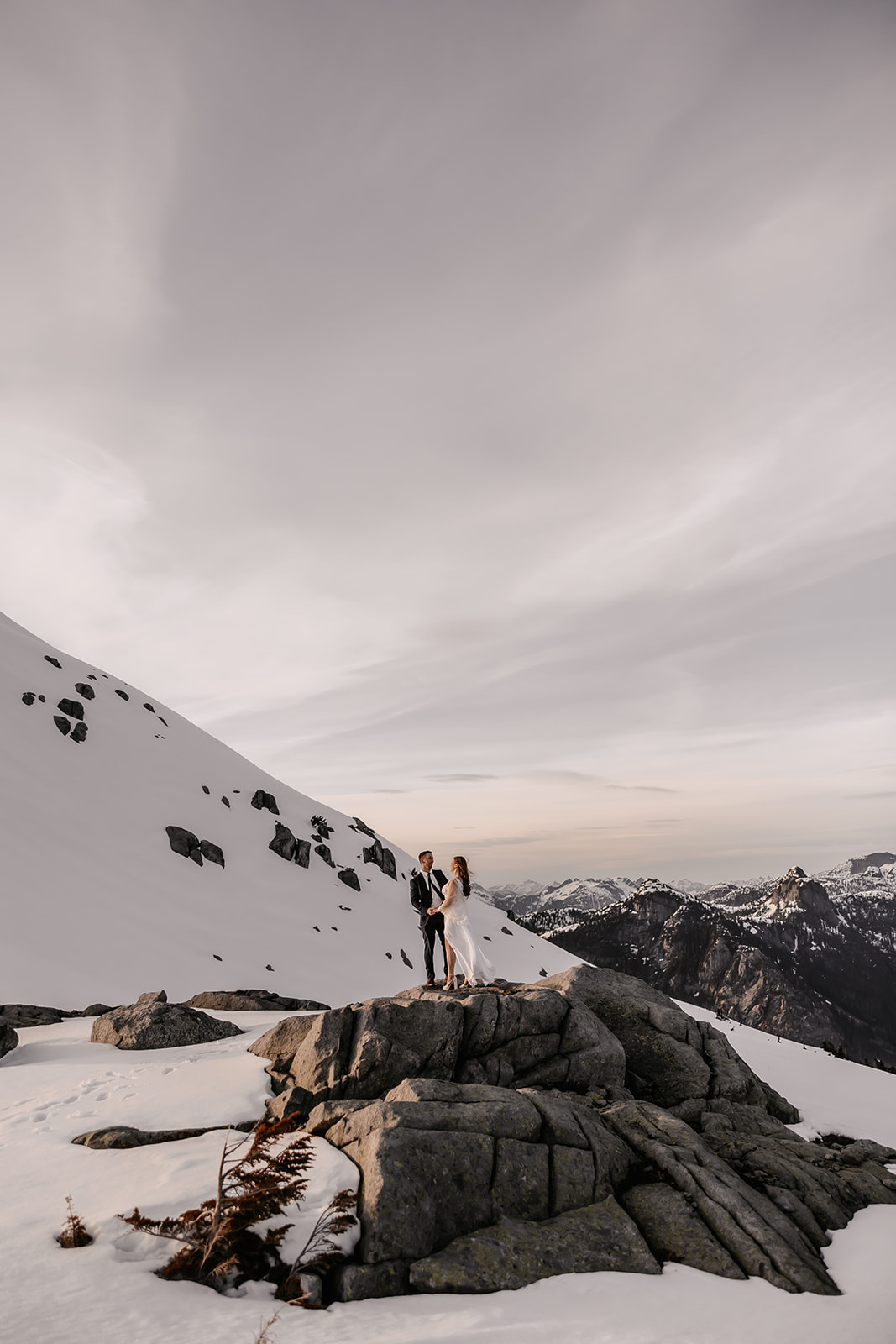 The bride and groom standing on a rocky outcrop, gazing into each other's eyes, surrounded by a pristine snowy landscape that enhances the magic of their helicopter elopement.