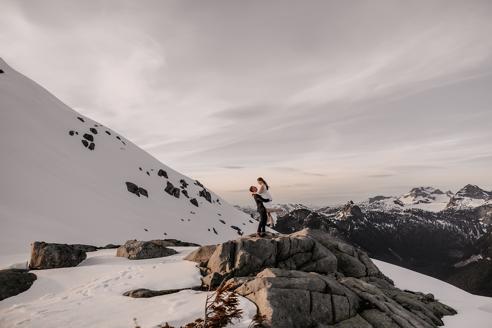 The couple joyfully celebrating their love, with the bride being lifted by her groom, framed by the stunning mountain scenery during their helicopter elopement.