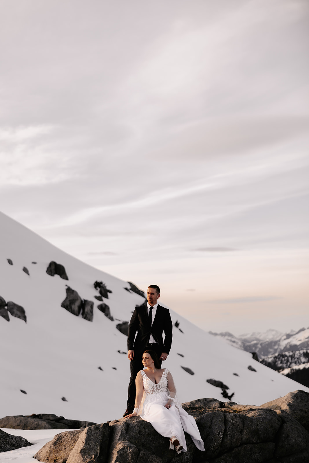 The bride and groom standing on a rocky outcrop, surrounded by a pristine snowy landscape that enhances the magic of their helicopter elopement.