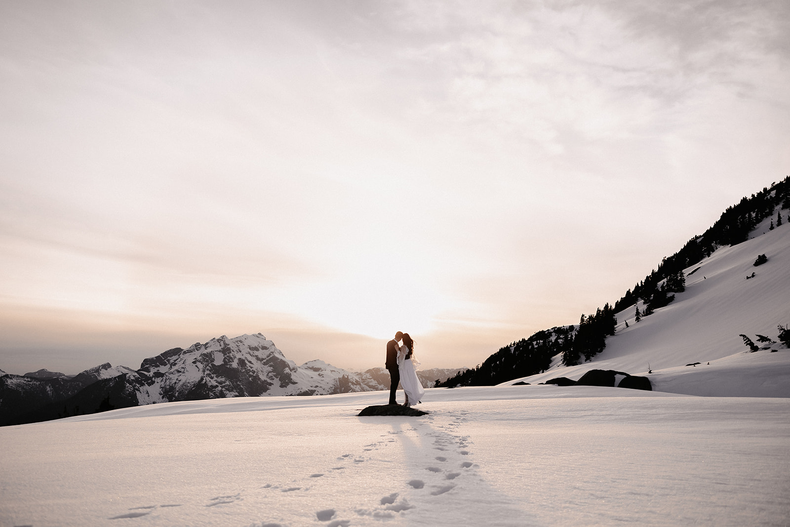 The couple sharing a romantic kiss as they stand together on a snow-covered mountain, encapsulating the intimate moments of their helicopter elopement.