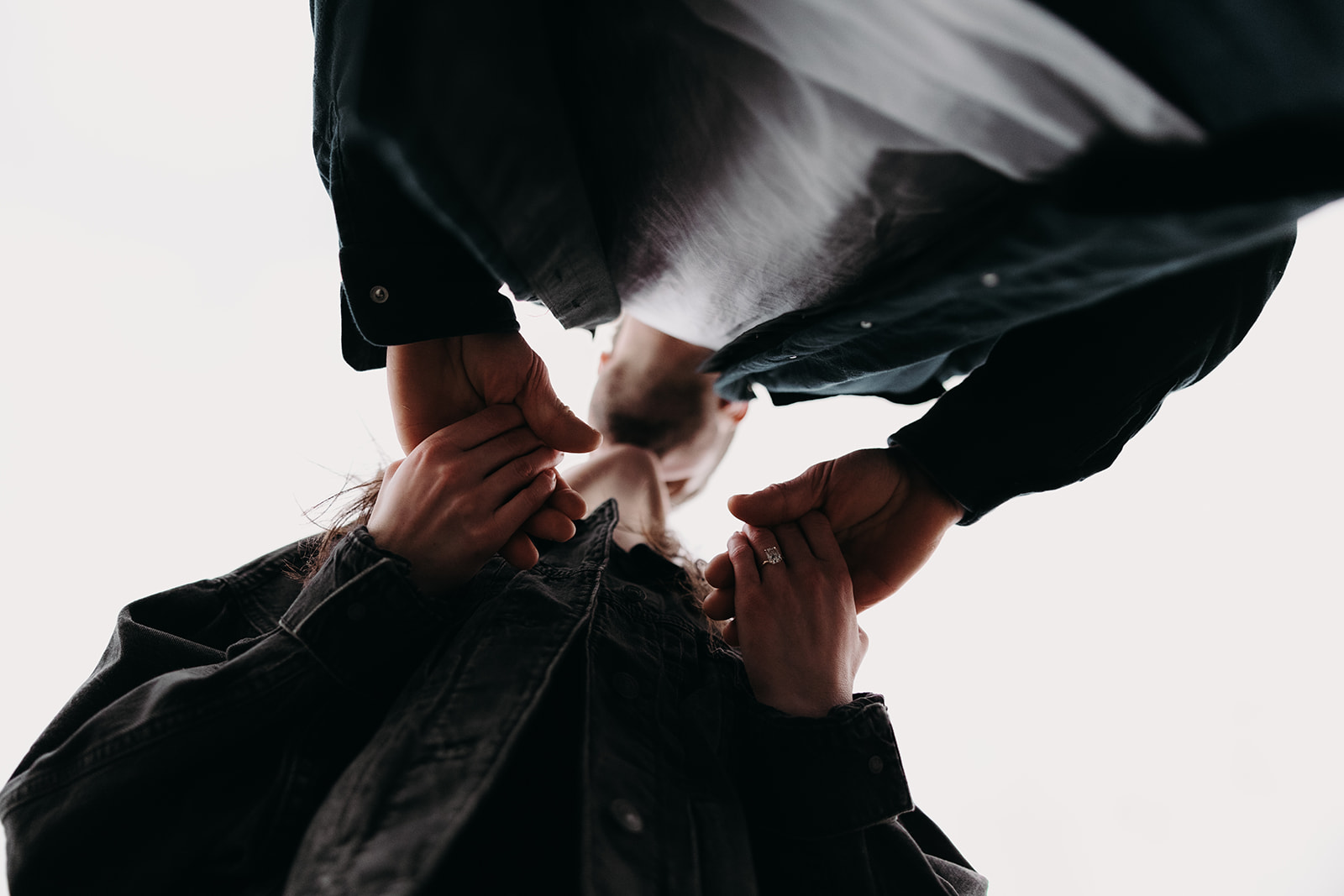 A close-up shot captures the couple holding hands, their fingers intertwined. The focus is on their hands, showcasing the woman's engagement ring glimmering softly. The couple leans in for a kiss, their faces slightly blurred but radiating joy and affection. This image beautifully highlights the intimate connection and emotion often found in fall engagement photos.

