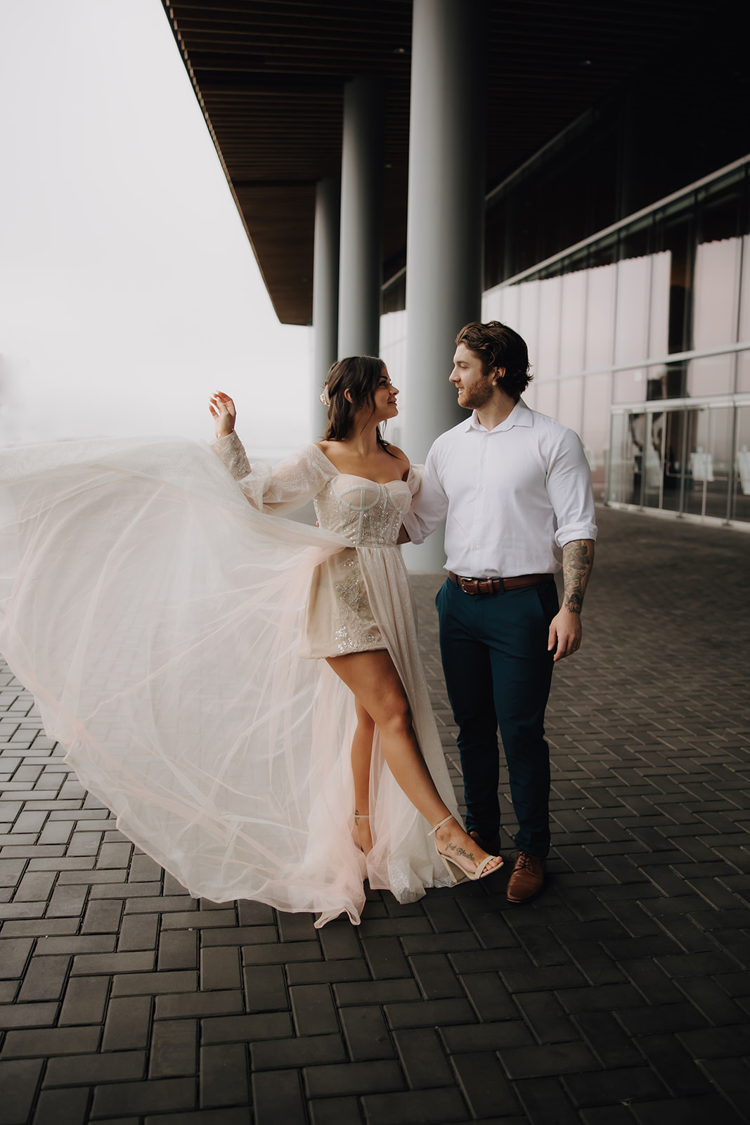 A couple sharing a sweet moment during their Vancouver elopement, surrounded by modern architecture in Coal Harbour. The bride twirls in her stunning gown, while the groom admires her.