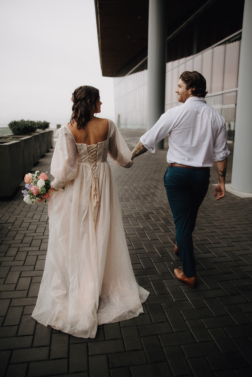 A close-up of the couple walking hand in hand during their Vancouver elopement in the city, with the bride’s gown trailing behind her, showcasing the urban landscape.