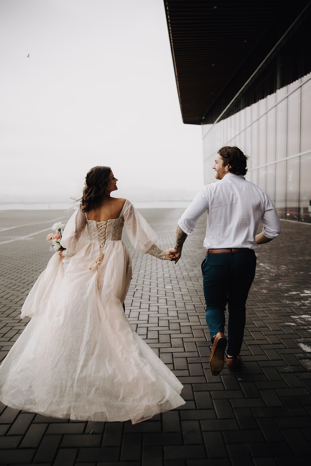 A close-up of the couple walking hand in hand during their Vancouver elopement in the city, with the bride’s gown trailing behind her, showcasing the urban landscape.