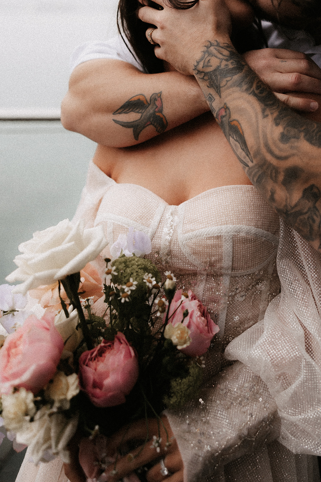 Close-up of a couple embracing, with the bride holding her bouquet of roses and the groom’s tattoos visible on his arm during their Vancouver Elopement.