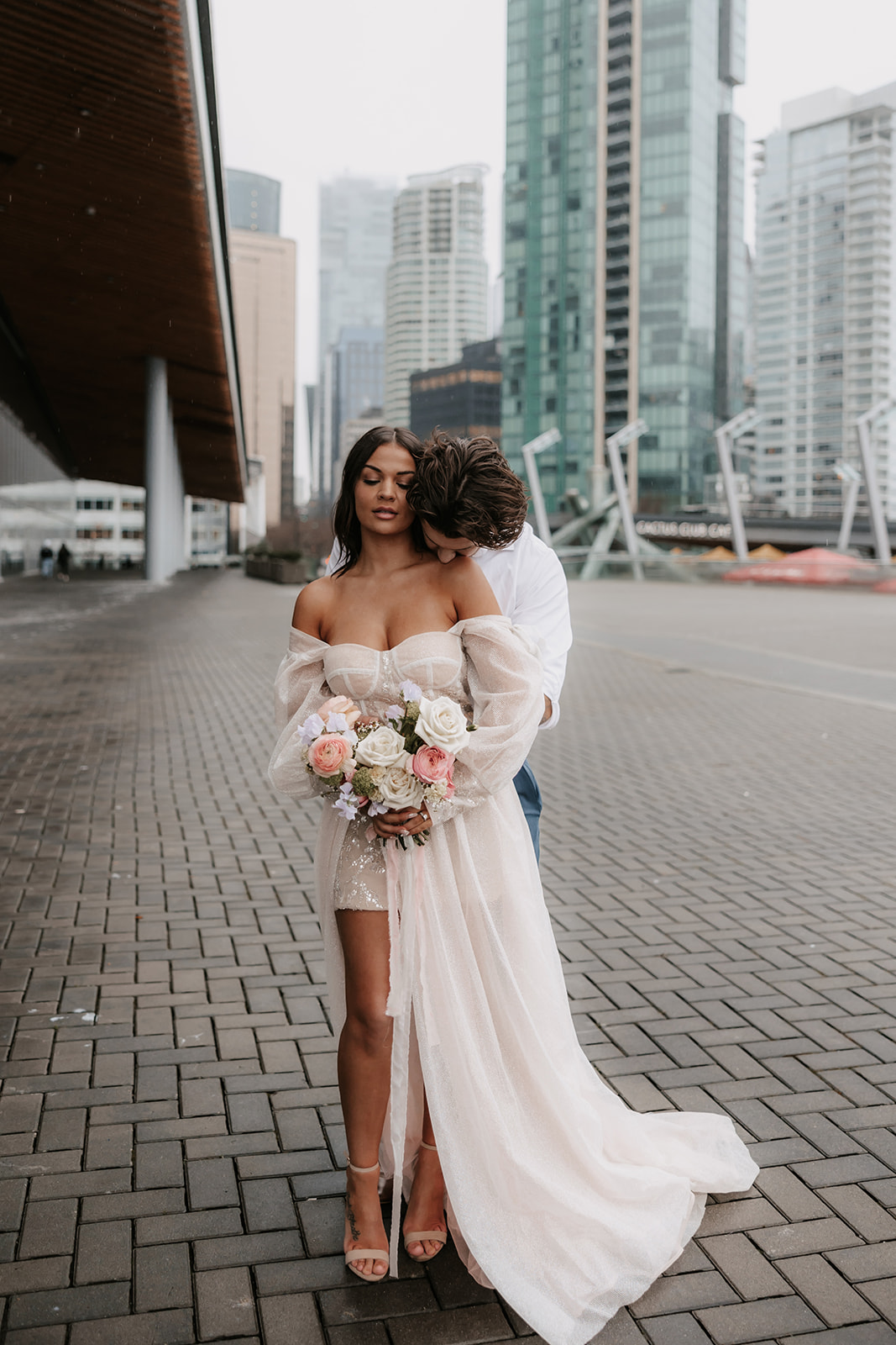 Couple in downtown Vancouver sharing a romantic moment under the architecture of the city, with the bride holding her bouquet of pink roses.