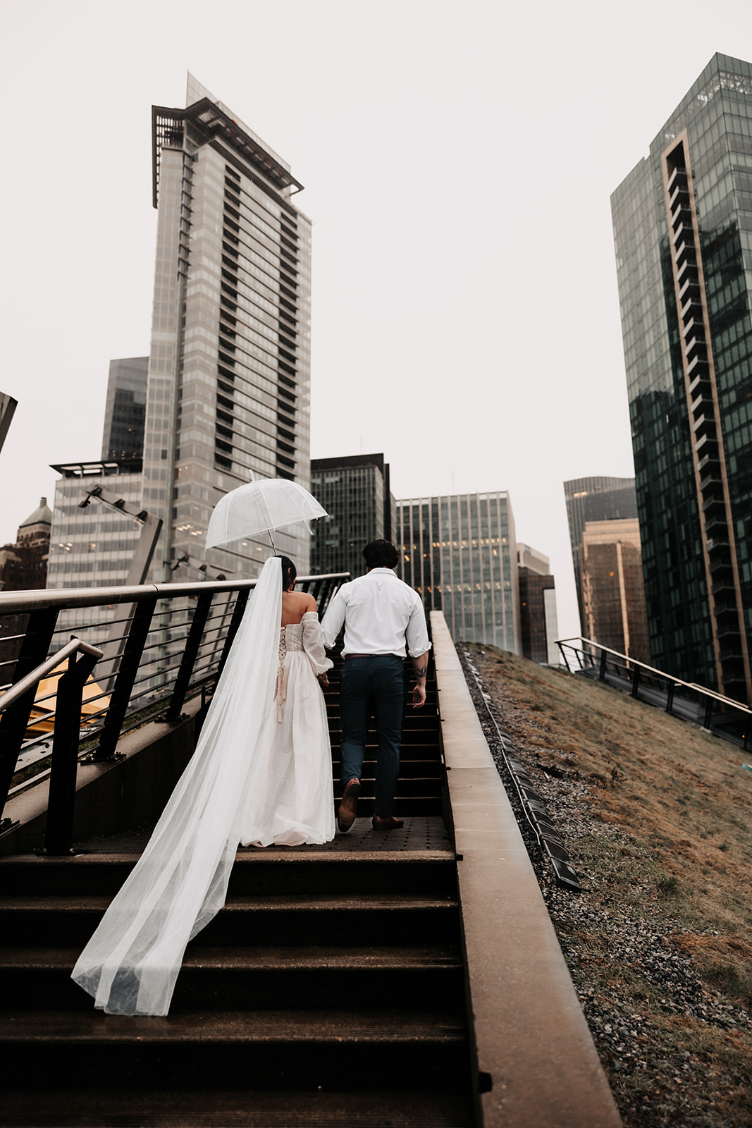 Bride and groom holding hands as they walk up stairs through downtown Vancouver during their Vancouver Elopement, surrounded by towering buildings.