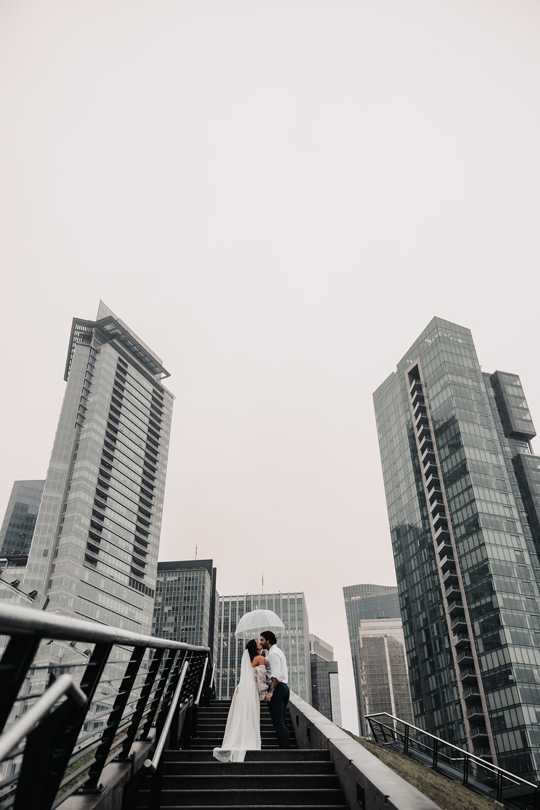 Bride and groom sharing a kiss while walking through downtown Vancouver during their Vancouver Elopement, surrounded by towering buildings.