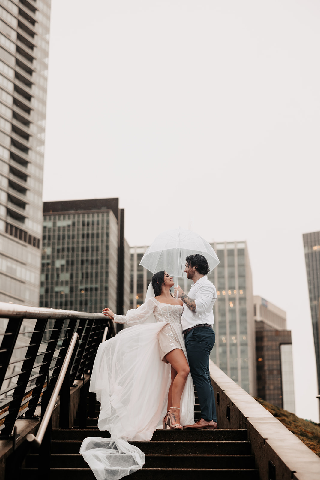 Bride and groom laughing together under an umbrella on a rainy day in Vancouver, with the Vancouver skyline as a backdrop during their elopement session.