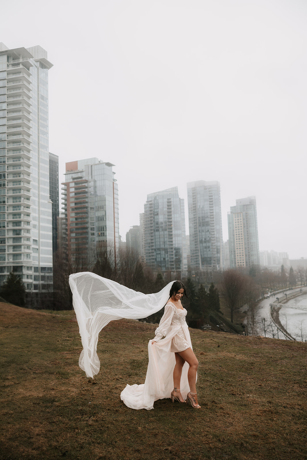 Bride enjoying a fun moment in her wedding gown, with the veil flowing in the wind in front of the Vancouver skyline during her elopement.