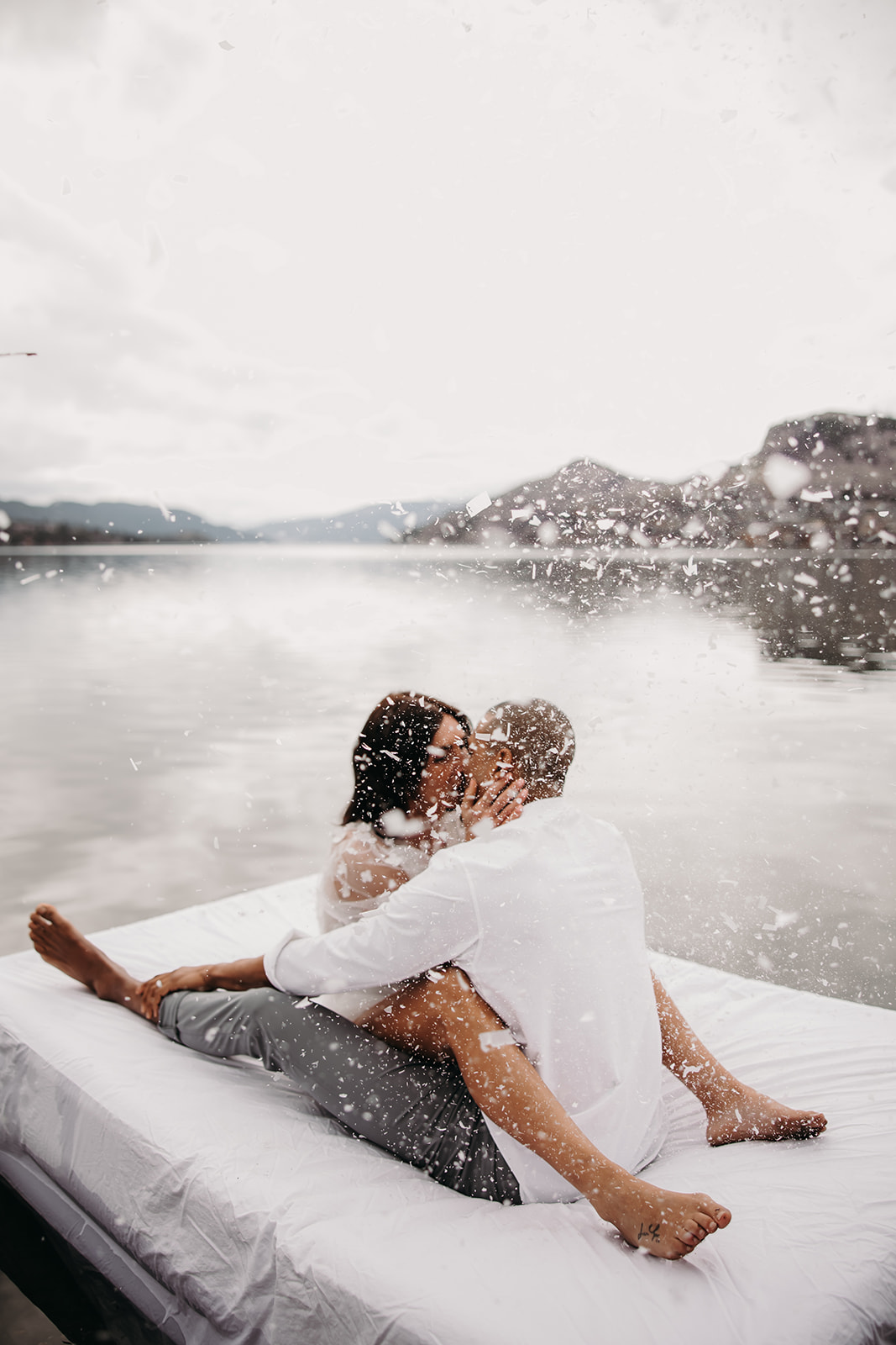 Couple kissing on a mattress floating on Kalamalka Lake during their Okanagan elopement. The lake's serene reflection and surrounding hills create a romantic atmosphere.