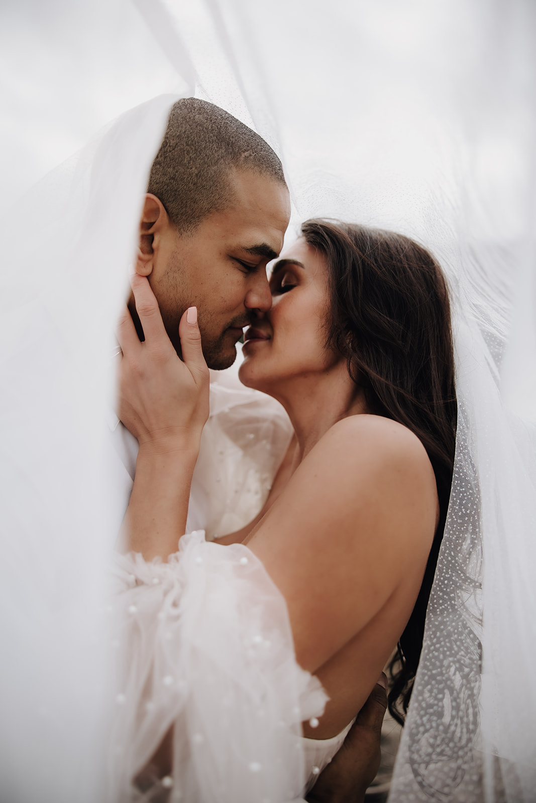 A close-up of the couple embracing, the bride's veil floating around them, capturing the intimate moment during their Okanagan elopement with the dramatic backdrop of the lake.