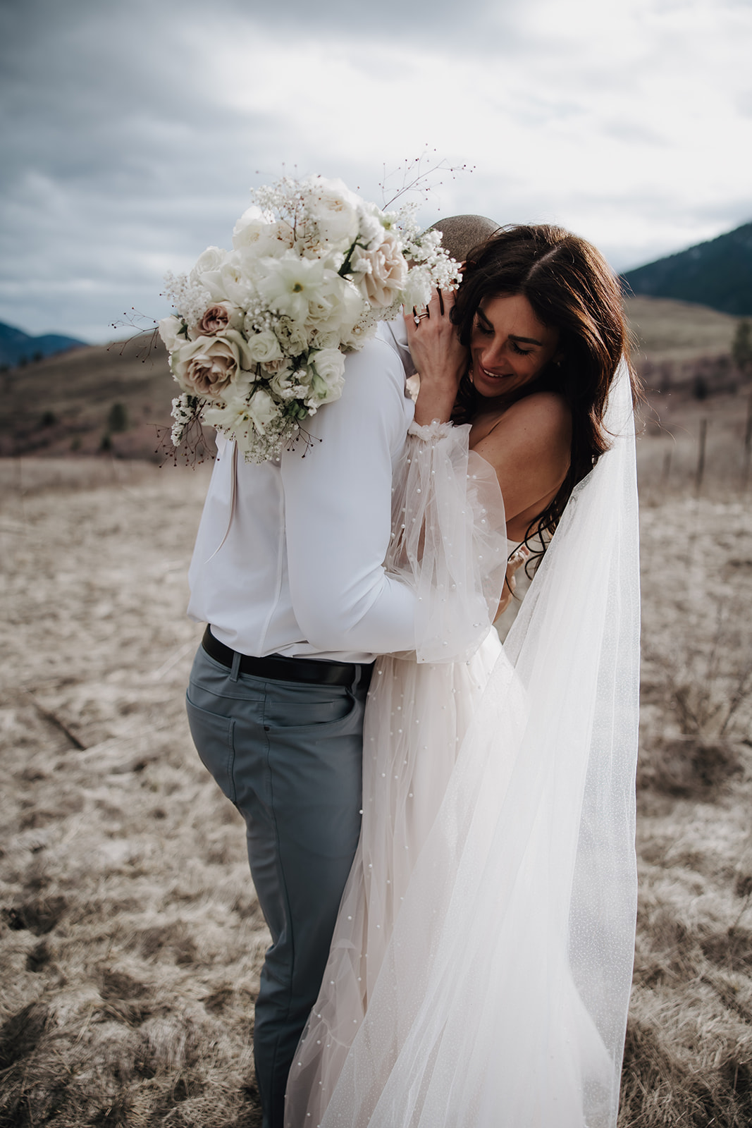 The couple laughs and embraces, with their stunning bouquet and the serene lake landscape completing the picturesque moment captured during their Okanagan elopement.