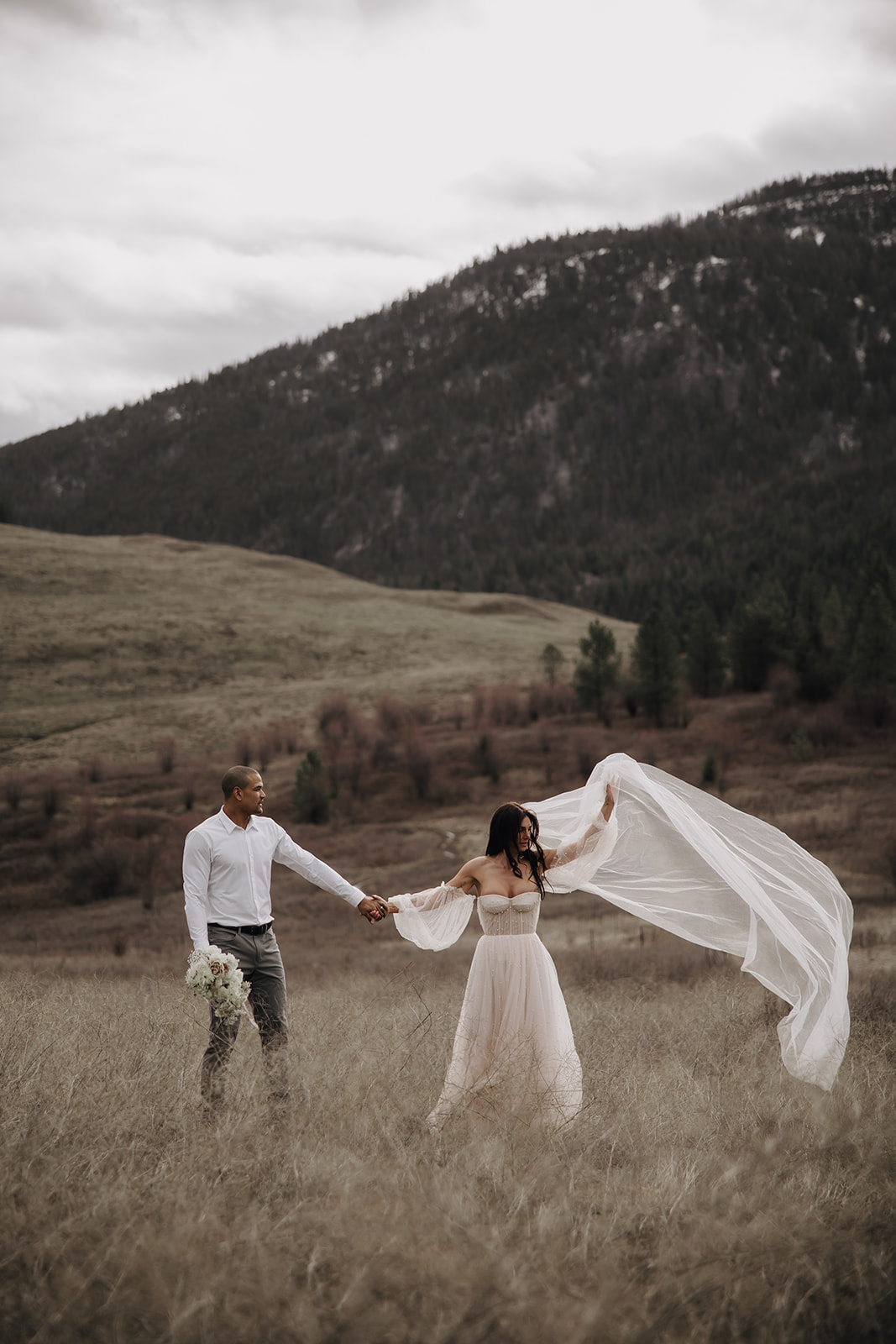 Couple playfully twirling in a scenic field during their Okanagan elopement. The mountains and lake provide a stunning backdrop for this adventurous moment.

