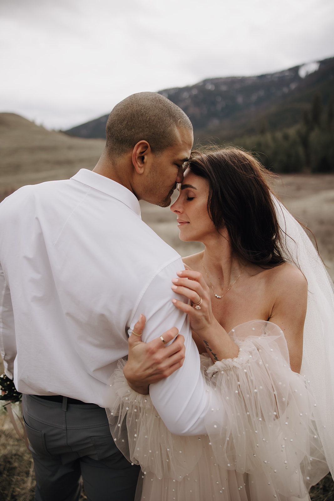 A romantic moment during an Okanagan elopement, where the couple shares a gentle forehead kiss, with a stunning mountain landscape in the background.