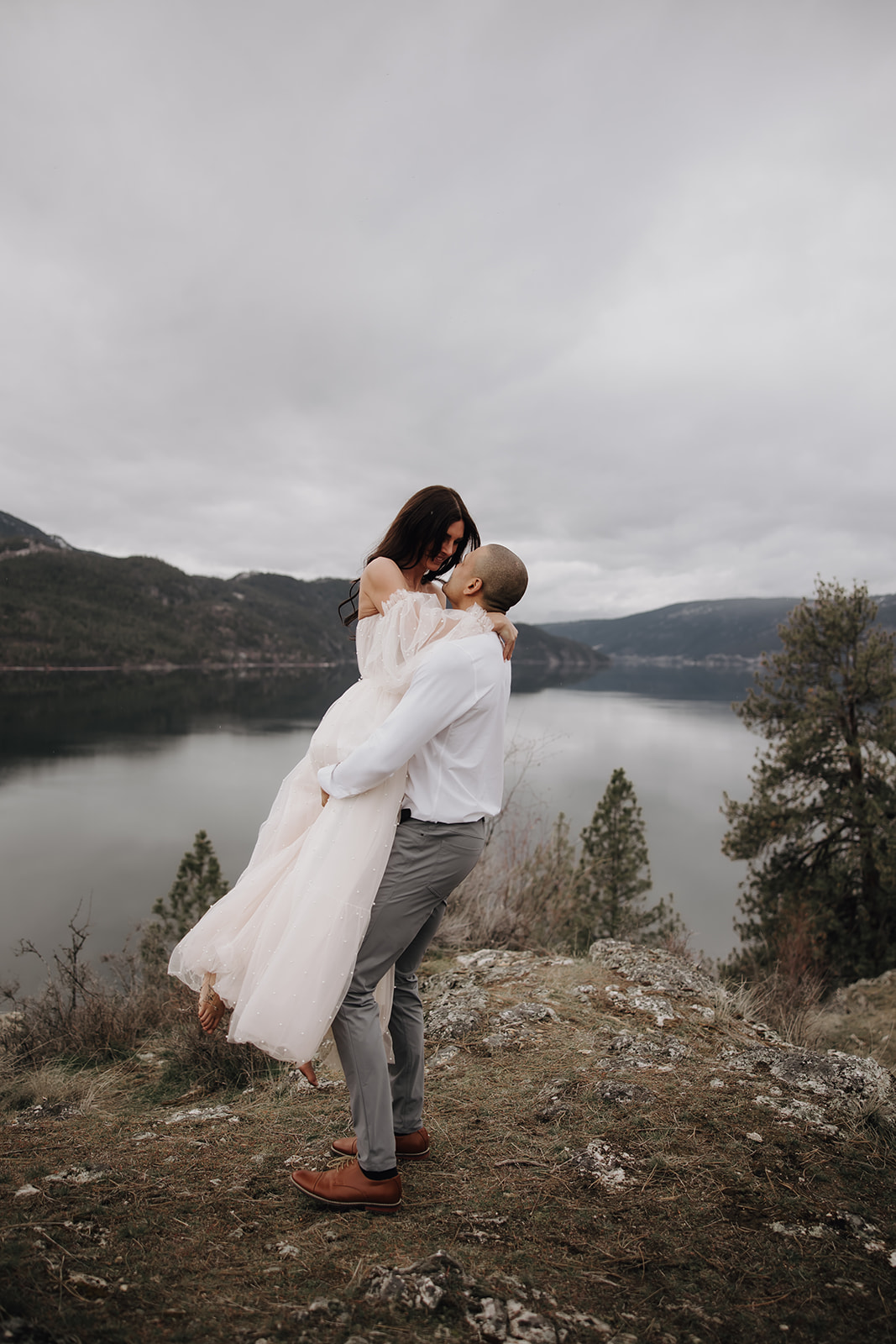 A joyful couple embraces on a cliffside, with the stunning Okanagan lake view in the background, showcasing the beauty of their adventure elopement.