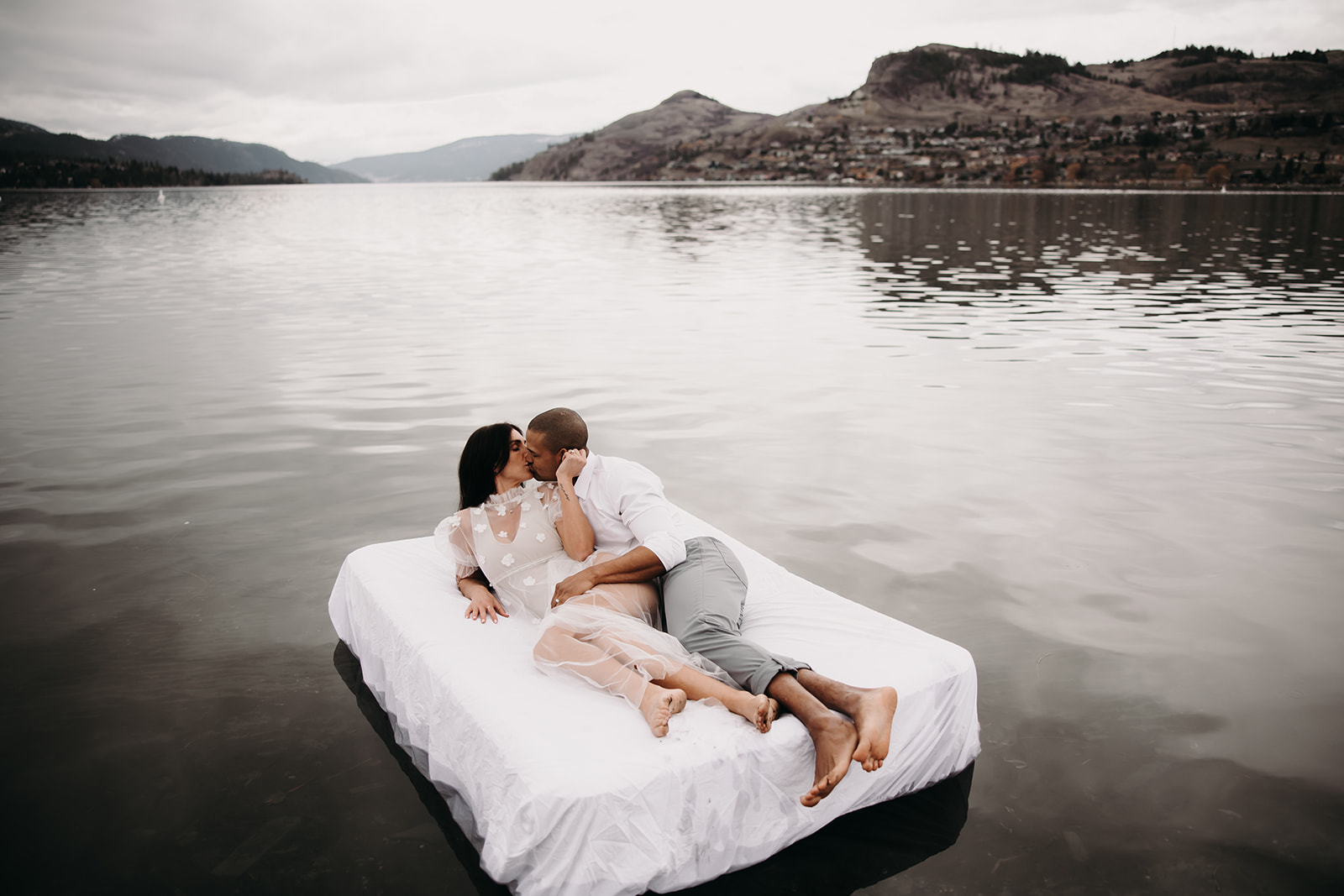 A couple snuggles on a float in the lake, surrounded by breathtaking Okanagan scenery, reflecting the peaceful beauty of their Okanagan elopement.