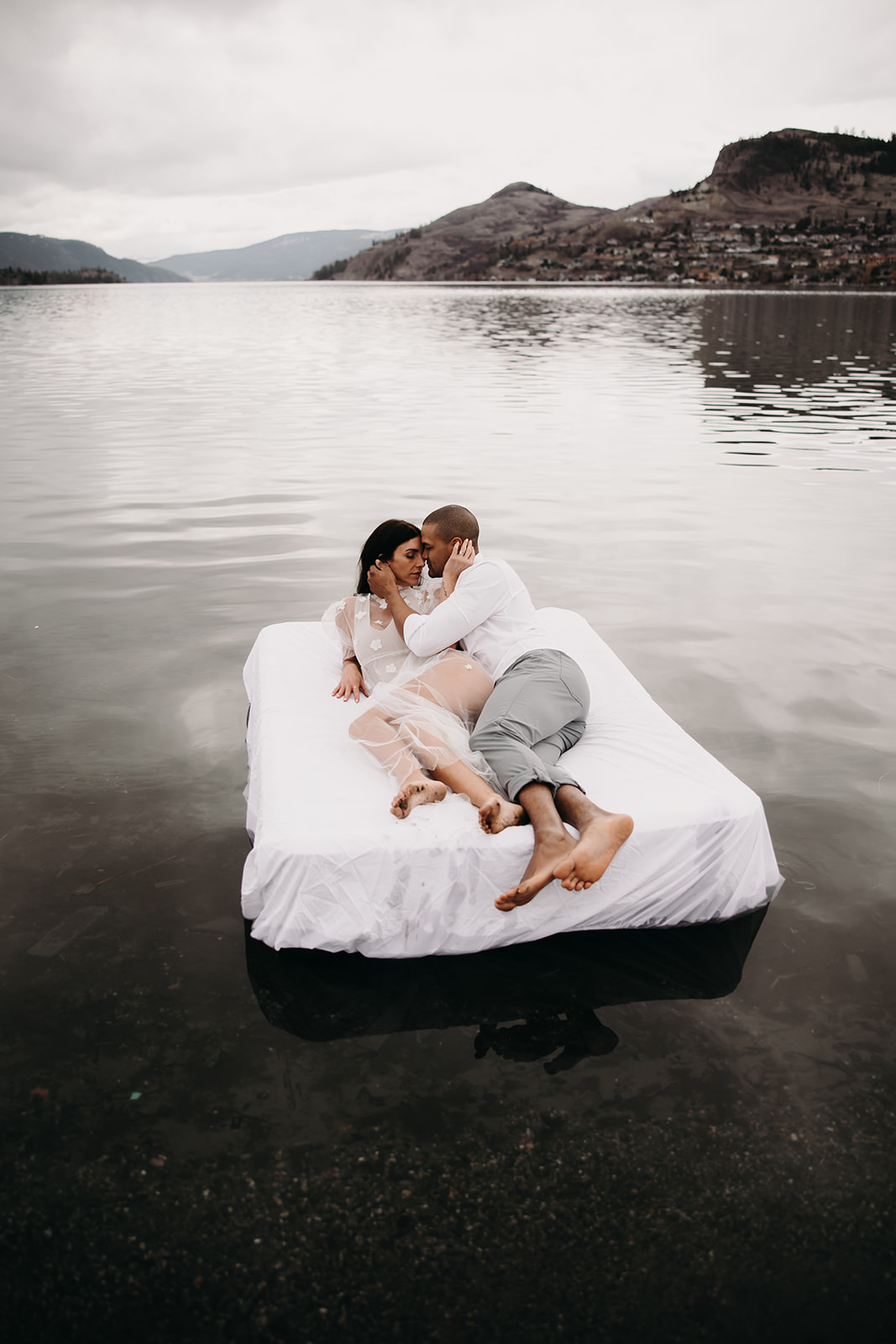 Unique engagement photo ideas captured in the serene calm of a lake, as this couple embraces on an air mattress, creating a memorable moment in the water.