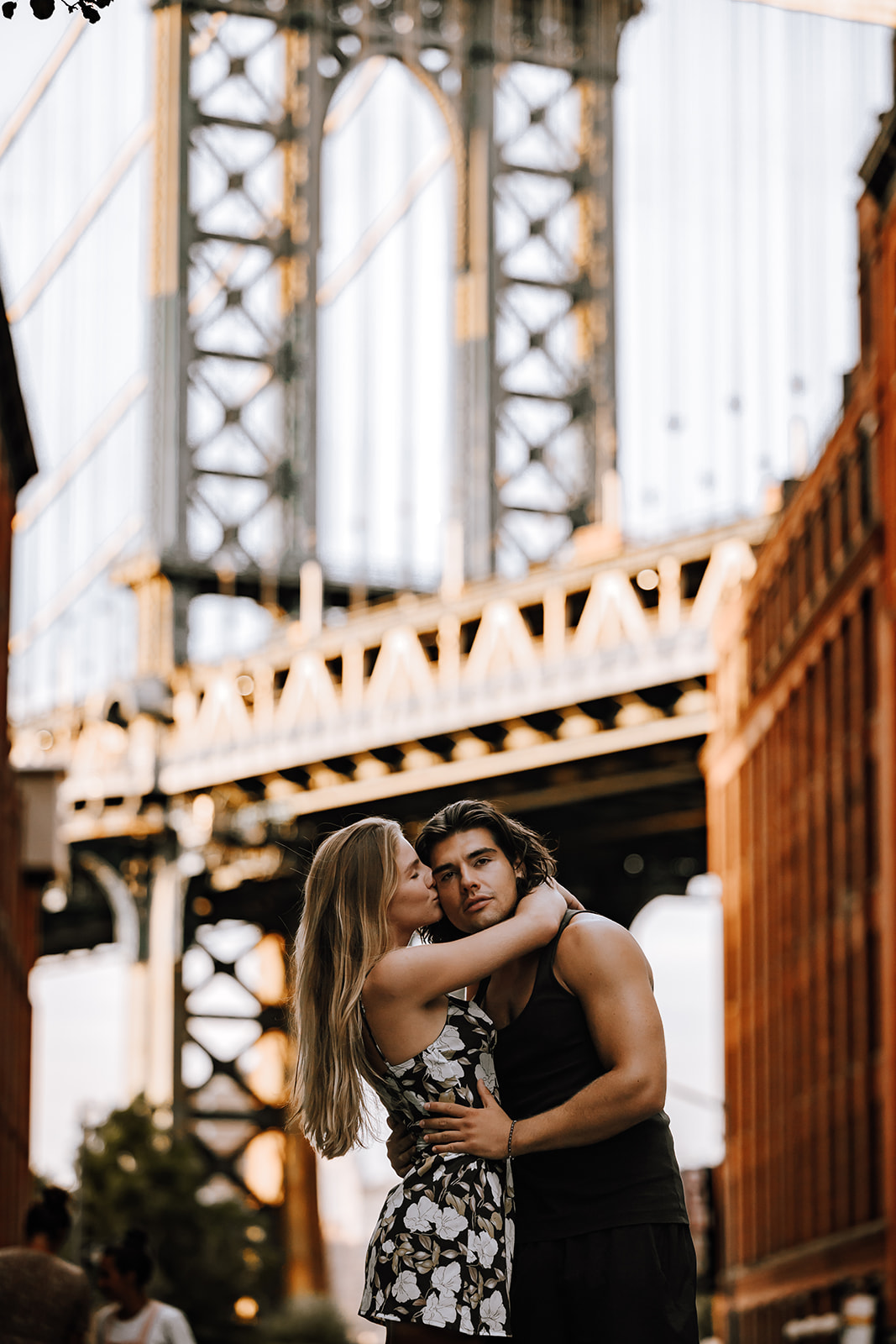 The couple playfully embracing each other with the Manhattan Bridge in the background during their new york city couple photoshoot, radiating happiness.

