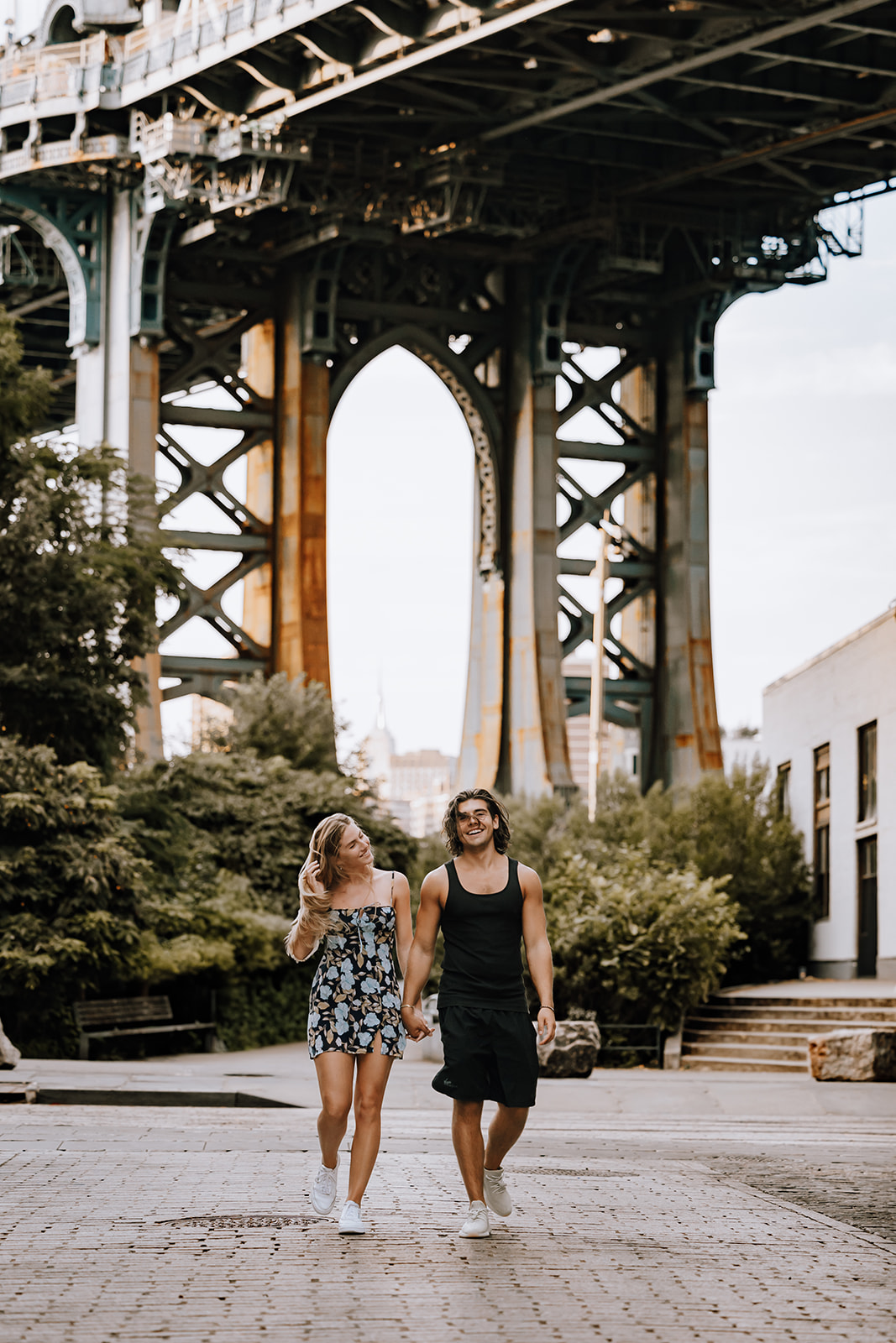 The couple walking hand in hand under the Manhattan Bridge, showcasing their carefree spirit during their city couple photoshoot.