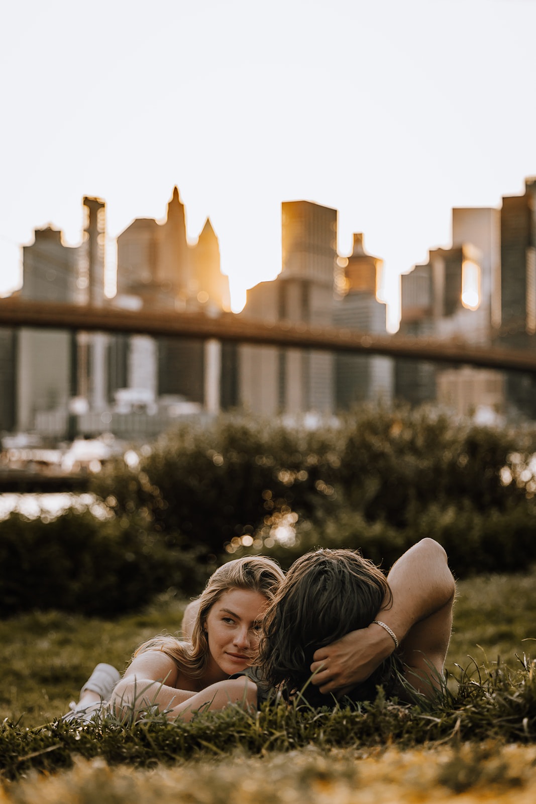 The couple relaxing on the grass with the skyline in the distance, showcasing a serene moment from their new york city couple photoshoot.