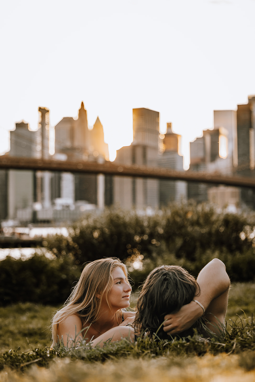 The couple relaxing on the grass with the skyline in the distance, showcasing a serene moment from their new york city couple photoshoot.